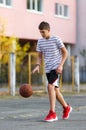 Cute boy in white t shirt plays  basketball on street  playground. Teenager  throws orange basketball ball outside. H Royalty Free Stock Photo
