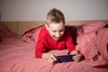 Cute boy before going to bed playing on the phone lying on the bed under the blanket Royalty Free Stock Photo