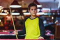 Cute boy in yellow t shirt plays billiard or pool in club. Young Kid learns to play snooker. Boy with billiard cue