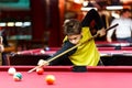 Cute boy in yellow t shirt plays billiard or pool in club. Young Kid learns to play snooker. Boy with billiard cue