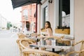 Cute brown-haired young girl sitting in a cafe outdoor, rattan chairs alone. No people around Royalty Free Stock Photo