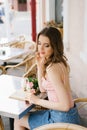 Cute brown-haired young girl sitting in a cafe outdoor, rattan chairs, reading an open book. Next to the table is a bouquet of ros Royalty Free Stock Photo