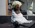 Cute brown mini poodle in a white towel and shower cap after washing in a grooming salon.
