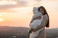 Cute brunette girl in beige dress hugs her samoed puppy, beautiful sunset on the background Royalty Free Stock Photo