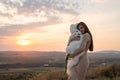 Cute brunette girl in beige dress hugs her samoed puppy, beautiful sunset on the background Royalty Free Stock Photo