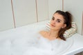 Cute brunette lies in the bath with foam and looks into the camera Royalty Free Stock Photo