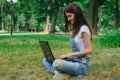 Cute brunette sits in a park on the lawn and prints on a laptop