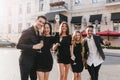 Cute brunette woman raising wineglass while her boyfriend hugging her on the street. Enthusiastic friends walking around Royalty Free Stock Photo