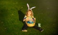 Cute bunny child boy with rabbit ears. Easter egg hunt in garden. Child boy playing in field, hunting easter eggs. Royalty Free Stock Photo