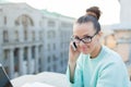 Cute businesswoman in glasses talking on phone and smiling while standing on the roof of the house in the old town. Next to it are Royalty Free Stock Photo