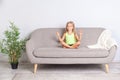 Cute calm little girl meditating in lotus pose with closed eyes sitting on couch at home, child doing mudra gesture Royalty Free Stock Photo