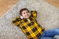 Cute carefree little boy resting on floor at home, listening to music via headphones and dreaming, top view, free space