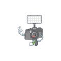 Cute cartoon mascot picture of photo camera with lighting with two fingers