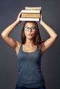 Cute and casual. Studio portrait of a young woman balancing a pile of books on her head against a grey background. Royalty Free Stock Photo