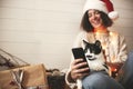 Cute cat looking at phone screen with funny emotions and sitting on happy girl legs in christmas lights. Young hipster woman in Royalty Free Stock Photo