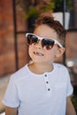 Cute cauasian boy in white tee shirt and sunglasses posing for camera and showing his lost tooth.