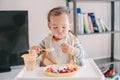 Cute Caucasian baby boy eating ripe berries and fruits with yogurt. Funny smiling child kid sitting in chair eating fresh berries