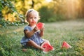 Cute Caucasian baby girl eating ripe red watermelon in park. Funny child kid sitting on ground with fresh fruit outdoors. Royalty Free Stock Photo