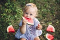 Cute Caucasian baby girl eating watermelon in park. Funny child kid sitting on ground with fresh fruit outdoors. Supplementary Royalty Free Stock Photo