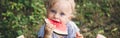 Cute Caucasian baby girl eating watermelon in park. Funny child kid sitting on ground with fresh fruit outdoors. Supplementary Royalty Free Stock Photo