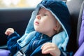 Cute Caucasian baby infant sitting in car seat. Adorable kid in outwear clothes in automobile vehicle carsit fastened with