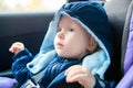 Cute Caucasian baby infant sitting in car seat. Adorable kid in outwear clothes in automobile vehicle carsit fastened with