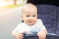 Cute caucasian blond curious baby boy sitting in stroller , smiling, looking and aspiring to something outdoor at city park.