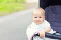 Cute caucasian blond curious baby boy sitting in stroller , smiling, looking and aspiring to something outdoor at city park.