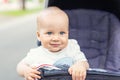 Cute caucasian blond curious baby boy sitting in stroller , smiling, looking and aspiring to something outdoor at city park. Royalty Free Stock Photo