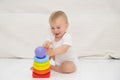 Cute caucasian blond smiling baby girl sitting alone on floor, playing with multi coloured pyramidion, light modern