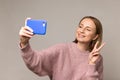 Young woman take selfie photo on smartphone showing peace V sign smile to camera over studio wall Royalty Free Stock Photo