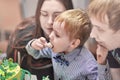 Cute caucasian blonde boy eats sweeties from the Birthday cake sitting between the parents. Royalty Free Stock Photo