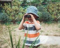 cute Caucasian boy in stripped tshirt and hat looking through binoculars