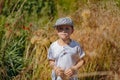 Cute Caucasian boy wearing white tee shirt and checkered baseball cap, standing in yellow green grass field with red flowers. Royalty Free Stock Photo