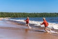 Cute caucasian boys wearing red hoodies and blue underpants running from waves