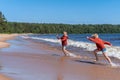 Cute caucasian boys wearing red hoodies and blue underpants running from waves in Ladoga lake with enthusiasm.