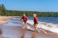 Cute caucasian boys wearing red hoodies and blue underpants running from waves in Ladoga lake with enthusiasm. Royalty Free Stock Photo