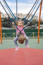 Cute caucasian child girl swinging on a swing on a children`s playground