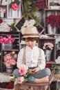 Cute Caucasian child sitting on a stool, surrounded by a bouquets of roses Royalty Free Stock Photo