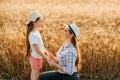 Cute caucasian farmer family with hat little girl and her mother holding hands and talking in wheat field. Royalty Free Stock Photo