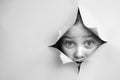 Cute Caucasian girl peeks out of a hole in a paper background.