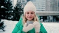 A cute caucasian girl in warm clothes drinks hot tea from a mug while walking in a snowy city park. Royalty Free Stock Photo