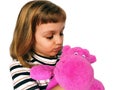 A cute Caucasian girl of 7 years old with blond hair cuddles and hugs a pink hippopotamus. Hippo plush toy. An Royalty Free Stock Photo