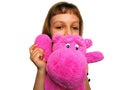 A cute Caucasian girl of 7 years old with blond hair cuddles and hugs a pink hippopotamus. Hippo plush toy. An Royalty Free Stock Photo