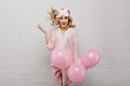 Cute caucasian lady in sleepmask jumping on white background with party balloons. Studio shot of amazed attractive