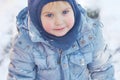 Cute caucasian liittle boy with bright blue eyes in winter clothes and hat hood on winter background. Healthy childhood. Outdoor