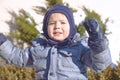 Cute caucasian liittle boy with bright blue eyes in winter clothes and hat hood on green pine and fir background. Healthy childh Royalty Free Stock Photo