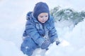 Cute caucasian liittle boy with bright blue eyes in winter clothes and hat hood plays with snow, laughing. Healthy childhood. Royalty Free Stock Photo