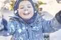 Cute caucasian liittle boy with bright blue eyes in winter clothes and hat hood plays with snow, laughing. Healthy childhood. Ou