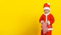 Cute caucasian little boy in a festive Santa Claus costume stands with an open sack of New Year`s gifts